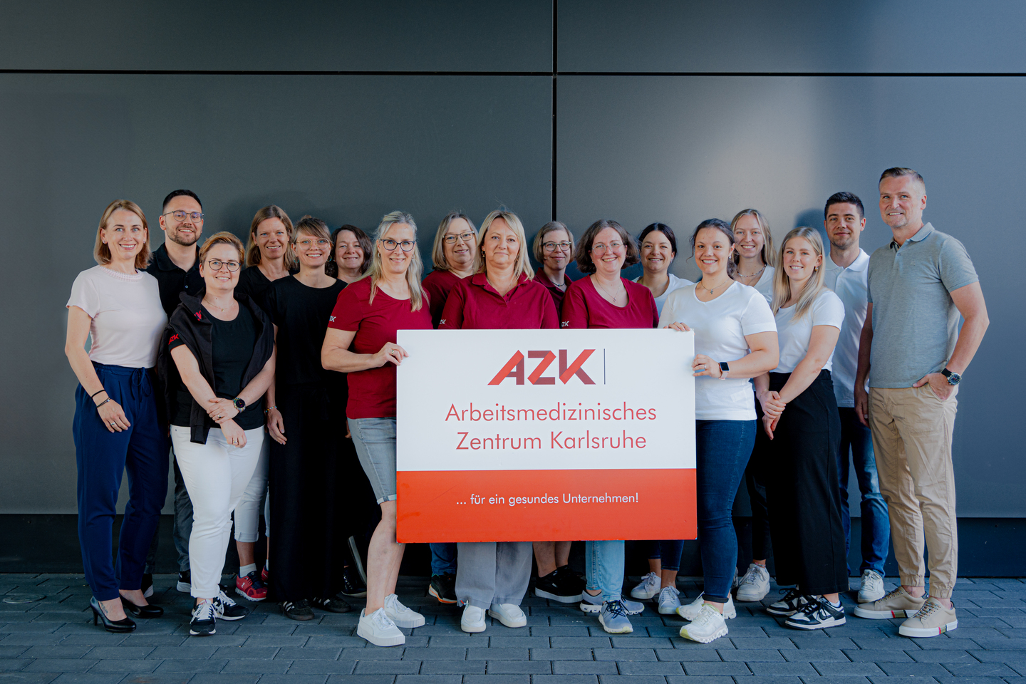 Gruppe von Menschen steht vor einem Schild mit der Aufschrift "AZK Arbeitsmedizinisches Zentrum Karlsruhe – für ein gesundes Unternehmen".